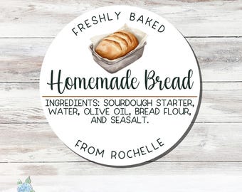 May include: A round white sticker featuring a watercolor illustration of a loaf of bread in a metal pan. Text reads: FRESHLY BAKED, Homemade Bread, INGREDIENTS: SOURDOUGH STARTER, WATER, OLIVE OIL, BREAD FLOUR, AND SEASALT, FROM ROCHELLE.