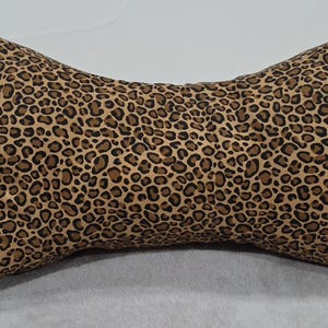 May include: A bone-shaped plush toy featuring a brown and black leopard print pattern. The soft, stuffed item has a distinct dog bone silhouette with rounded ends and a narrow center, constructed from fabric with a repeating animal spot design.