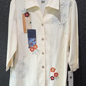 May include: A white ceramic mug with a black handle and the text "But First, Coffee" in a bold, black font. The mug is set against a blurred background, highlighting its clean design.