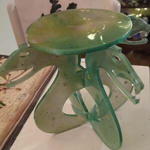 Puede incluir: Una escultura de serpiente de tres cabezas de plástico translúcido verde con una parte superior redonda y plana. La escultura está hecha de plástico y tiene una superficie texturizada moteada.