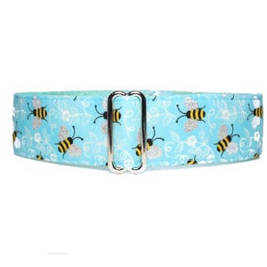 May include: A light blue dog collar featuring a repeating pattern of yellow and black bees with silver glitter wings and white floral accents. The collar has a silver metal buckle.