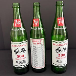 May include: Three green glass 7up souvenir bottles, each with a 16 fluid ounce capacity. The labels feature the Indianapolis 500 logo, checkered flags, and the date May 28, 1978. One bottle displays a list of winners of the 500 race on its label.