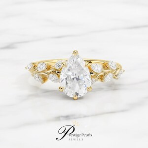 Stunning 2 carat pear shaped moissanite engagement ring in yellow gold, detailed with a diamond leaf vine band, vintage floral design symbolizing love, growth, and timeless natural beauty.