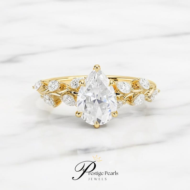Stunning 2 carat pear shaped moissanite engagement ring in yellow gold, detailed with a diamond leaf vine band, vintage floral design symbolizing love, growth, and timeless natural beauty.