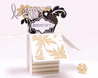 May include: A pop-up card with a gold and white floral design. The card is open and the pop-up features a black and white floral design with the words "happy anniversary".