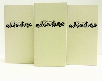 May include: Three brown notebooks with the text "life's an adventure" printed in black on the front.