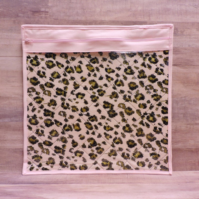 Peut inclure: Une pochette zipp&eacute;e rose avec un devant en vinyle transparent orn&eacute; d'un motif l&eacute;opard matelass&eacute;.