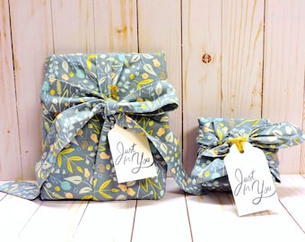 May include: Two rectangular packages wrapped in blue fabric featuring a yellow, white, and light blue botanical leaf pattern. Each package is tied with a fabric knot and includes a white rectangular gift tag with the text Just for You.