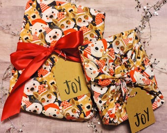 May include: Two wrapped gifts with a festive pattern of cartoon animals wearing Santa hats and scarves. The gifts are tied with red satin ribbons and have brown tags that read "JOY".