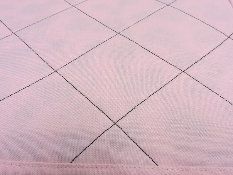 Peut inclure: Gros plan sur un tissu rose avec un motif en losange cousu avec du fil noir.