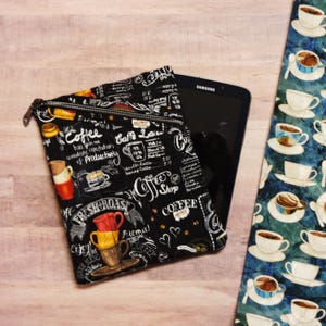 May include: Black zippered pouch with a coffee shop theme print. The print features coffee cups, coffee beans, and the text "Coffee has given me wonderful expectations of productivity".