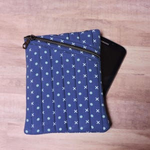 Könnte beinhalten: Eine blaue gesteppte Tablethülle mit Reißverschluss und einem weißen und blauen Tupfenmuster. Die Hülle ist mit einem schwarzen Tablet darin abgebildet.