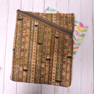 May include: A brown zippered pouch with a ruler print design. The pouch is open and has a notebook inside.