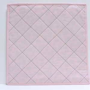 Peut inclure: Un tissu matelass&eacute; rose avec un motif en losanges cousu avec du fil noir. Le tissu a une texture douce et lisse.
