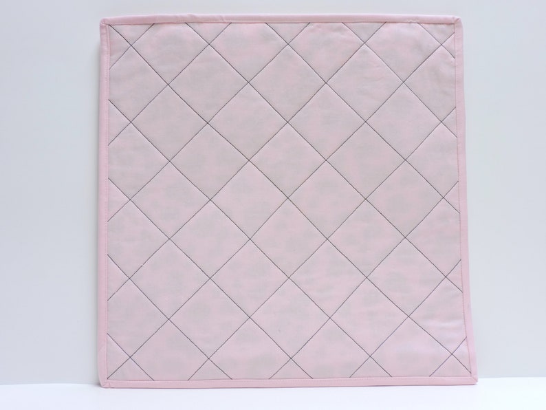 Peut inclure: Un tissu matelass&eacute; rose avec un motif en losanges cousu avec du fil noir. Le tissu a une texture douce et lisse.