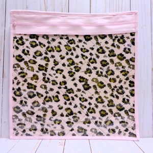Peut inclure: Pochette zipp&eacute;e rose avec un devant en vinyle transparent pr&eacute;sentant un tissu matelass&eacute; &agrave; imprim&eacute; l&eacute;opard rose et noir.