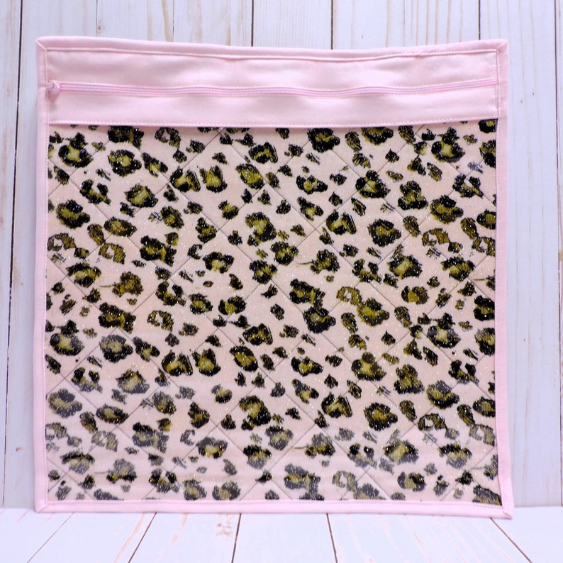Peut inclure: Pochette zipp&eacute;e rose avec un devant en vinyle transparent pr&eacute;sentant un tissu matelass&eacute; &agrave; imprim&eacute; l&eacute;opard rose et noir.