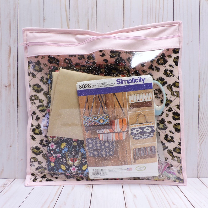 Peut inclure: Un sac &agrave; fermeture &eacute;clair rose avec un devant en vinyle transparent. Le sac contient des chutes de tissu, un patron de couture Simplicity et une tasse bleue. Le patron est pour des sacs et est &eacute;tiquet&eacute; "8028 os".