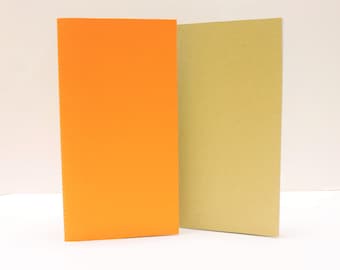 May include: Two notebooks, one orange and one brown, are side by side on a white surface. Both notebooks have a stitched binding.