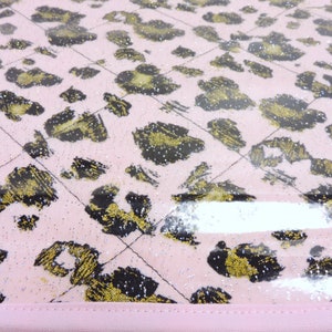 Peut inclure: Tissu rose avec un motif l&eacute;opard noir et or. Le tissu est recouvert d'une feuille de plastique transparente.