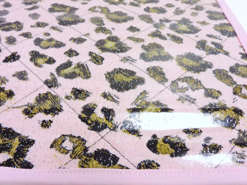 Peut inclure: Tissu rose avec un motif l&eacute;opard noir et or. Le tissu est recouvert d'une feuille de plastique transparente.
