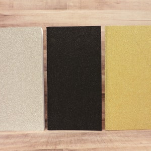 Puede incluir: Tres cuadernos con tapas de brillantina. Los cuadernos son plateados, negros y dorados.