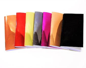 May include: A set of eight small notebooks with different colored covers. The covers are shiny and have a metallic finish. The colors are copper, red, gold, gray, magenta, peach, and black.