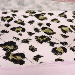 Peut inclure: Un tissu matelass&eacute; rose avec un motif l&eacute;opard noir et or. Le tissu a une fermeture &eacute;clair le long du bord inf&eacute;rieur.