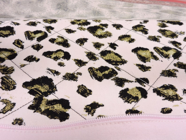 Peut inclure: Un tissu matelass&eacute; rose avec un motif l&eacute;opard noir et or. Le tissu a une fermeture &eacute;clair le long du bord inf&eacute;rieur.
