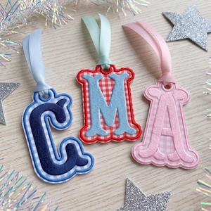 Puede incluir: Tres adornos colgantes bordados con las letras C, M y A. La C es azul marino con cuadros vichy azul claro, la M es azul claro con cuadros vichy rojos y la A es rosa con cuadros vichy rosa claro. Cada uno tiene un lazo de cinta de satén.