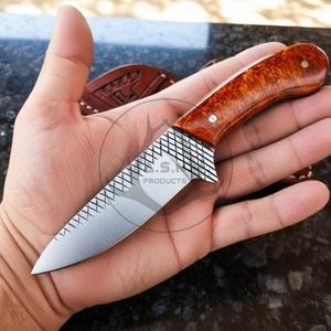 May include: A small, handcrafted knife with a polished, wooden handle and a silver blade. The handle is a warm, reddish-brown colour, and the blade has a textured pattern near the handle. The knife is held in a hand, showcasing its size and design.
