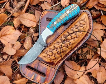 May include: A blue and brown patterned knife with a leather sheath. The knife has a Damascus steel blade and a decorative handle. The sheath is brown leather with a woven pattern.
