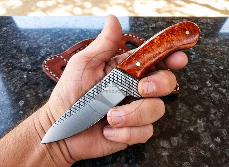 May include: A handcrafted knife with a wooden handle and a silver blade. The handle is a warm brown colour with a polished finish, and the blade has a textured pattern. A leather sheath is visible in the background.