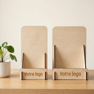 Peut inclure: Deux présentoirs en bois clair dotés d'un panneau arrière vertical et d'une petite étagère frontale. Chaque présentoir porte l'inscription "Votre logo" gravée sur le panneau avant. Les supports présentent des joints emboîtables aux bords sombres.