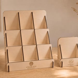 Peut inclure: Un présentoir en bois clair à neuf compartiments étagés et un plus petit présentoir en bois à un seul niveau. Les deux supports présentent des bords sombres et le texte ATELIER BOIS CREATIONS VIVANT imprimé sur les panneaux de base.