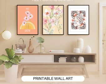 Op de afbeelding: Drie ingelijste bloemenprints met een licht perzikkleurige achtergrond. De prints hangen aan een lichtbeige muur boven een houten plank met boeken en decoratieve items. De tekst op de linker print luidt "Rise Grow". De tekst bovenaan de afbeelding luidt "All Posters 50% Off". De tekst onderaan de afbeelding luidt "Printable Wall Art".