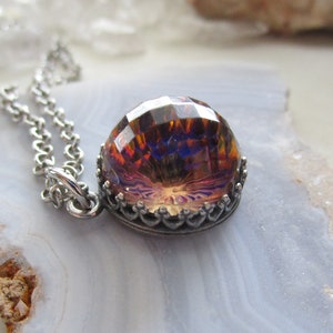 May include: A silver chain necklace with a large iridescent glass pendant. The pendant is faceted and has a crown-like setting.