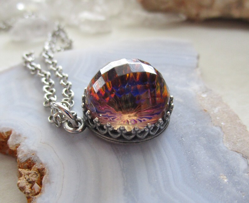 May include: A silver chain necklace with a large iridescent glass pendant. The pendant is faceted and has a crown-like setting.