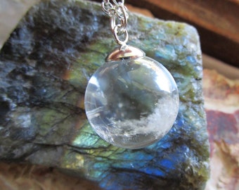 May include: A clear quartz crystal ball pendant on a silver chain. The pendant is hanging from a piece of iridescent labradorite.