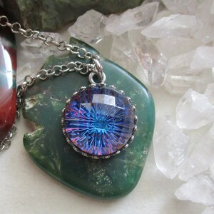 May include: A silver chain necklace with a round pendant featuring a blue and purple iridescent glass cabochon set in a silver bezel.