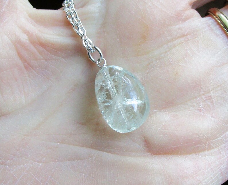 K&ouml;nnte beinhalten: Eine klare, tropfenf&ouml;rmige Anh&auml;ngerkette mit einer silbernen Kette. Der Anh&auml;nger hat eine durchscheinende, hellgr&uuml;ne Farbe mit inneren kristallinen Strukturen. Die Halskette ist ein Schmuckst&uuml;ck.