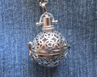 May include: A silver-colored pendant necklace featuring a spherical, openwork design. The pendant is composed of two halves that open to reveal a hollow interior. The necklace chain is also silver and appears delicate.