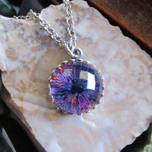 May include: A silver chain necklace with a round pendant featuring a purple and red iridescent glass eye with a black pupil.