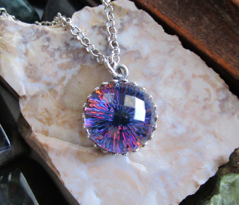 May include: A silver chain necklace with a round pendant featuring a purple and red iridescent glass eye with a black pupil.