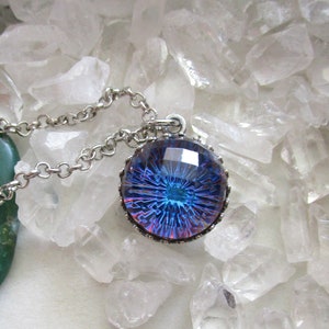 May include: A silver chain necklace with a round pendant featuring a blue and purple iridescent glass design. The pendant is set in a silver bezel with a decorative border.