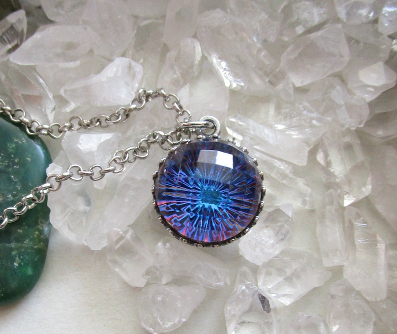 May include: A silver chain necklace with a round pendant featuring a blue and purple iridescent glass design. The pendant is set in a silver bezel with a decorative border.