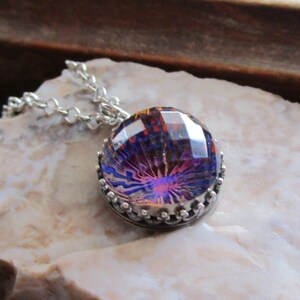 May include: A silver chain necklace with a round iridescent purple and orange glass pendant with a silver crown-like setting.