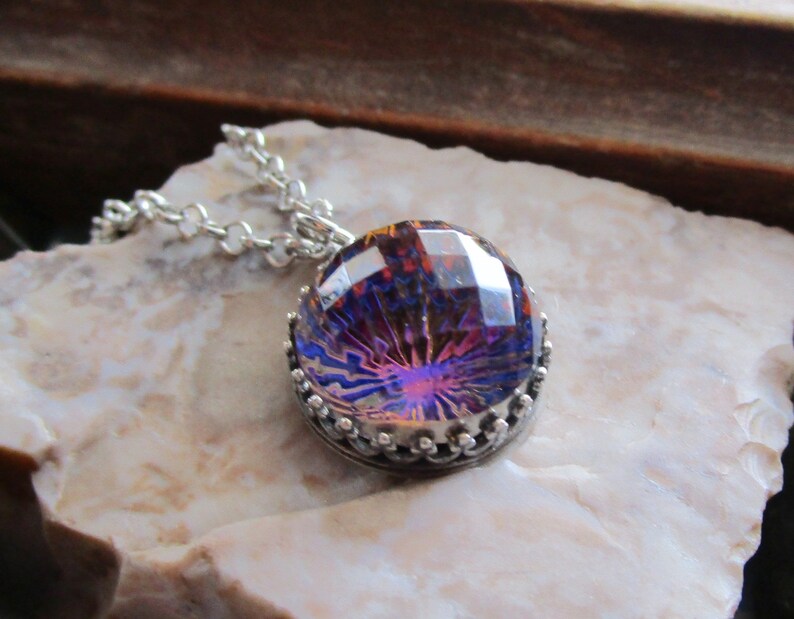 May include: A silver chain necklace with a round iridescent purple and orange glass pendant with a silver crown-like setting.