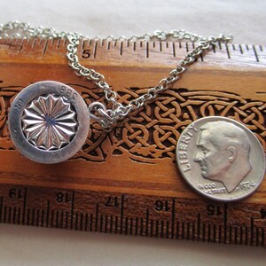 May include: A silver necklace with a round pendant featuring a stylized sunburst design and the inscription "1881" on the back. The pendant is about 1 inch in diameter and is hanging on a silver chain. A US dime is included for size comparison.