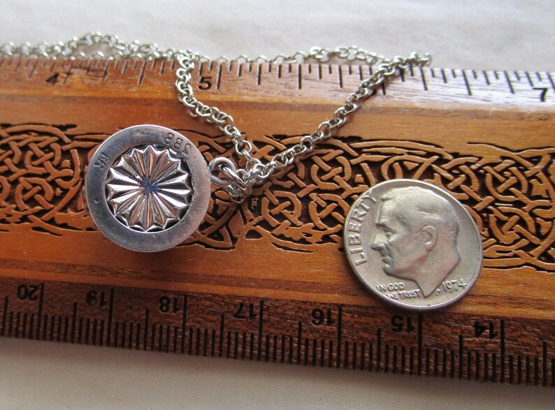 May include: A silver necklace with a round pendant featuring a stylized sunburst design and the inscription "1881" on the back. The pendant is about 1 inch in diameter and is hanging on a silver chain. A US dime is included for size comparison.